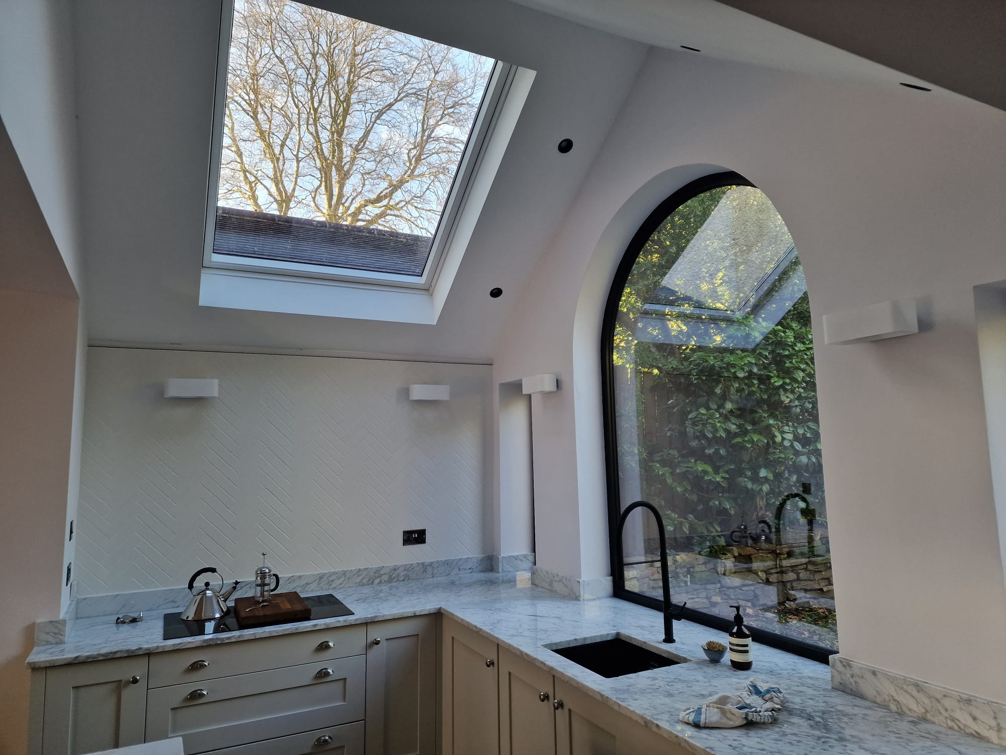 Premium fitted kitchen with marble worktops, butler sink with matt-black tap, vaulted ceiling, large skylight and tall arched garden window