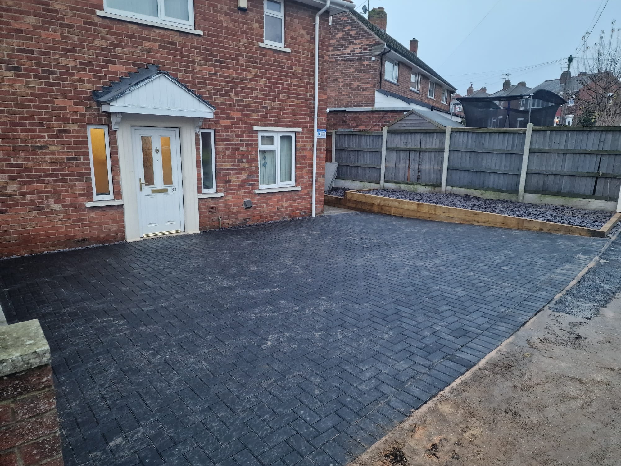 Charcoal block-paved driveway with railway-sleeper retaining border and slate-mulched bed at the front of a Yorkshire semi