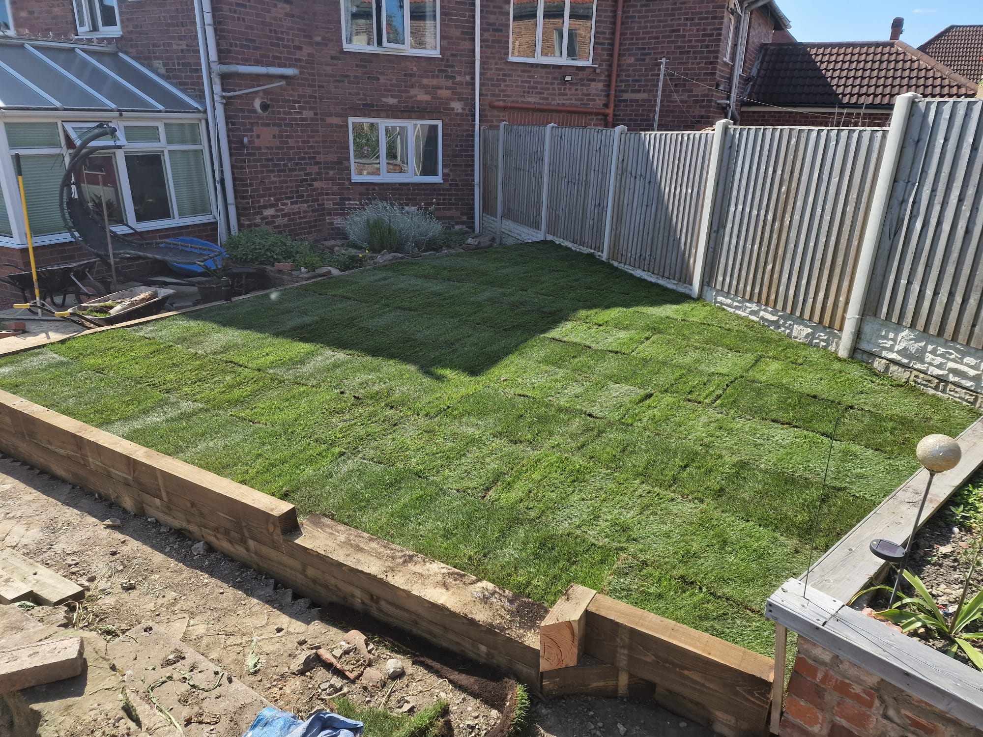 Newly laid turf rolls forming a sleeper-edged lawn between fenced borders in a Yorkshire family garden